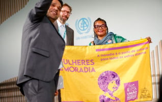 Maria das Graças Xavier unfurls a banner advocating for women’s right to housing at the WUF13 Dialogue on Informal Settlements. ©UN-Habitat/Ratmir Sherifov